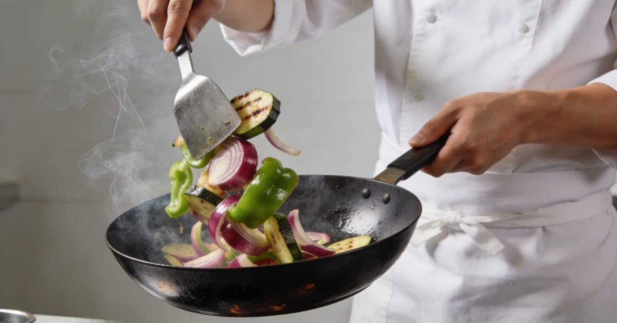 Chef faisant sauter legumes croquants dans wok fumant