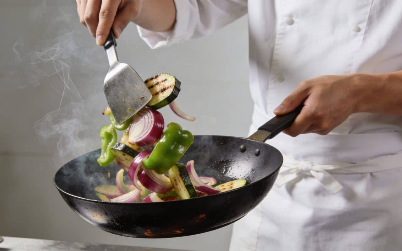 Chef faisant sauter legumes croquants dans wok fumant