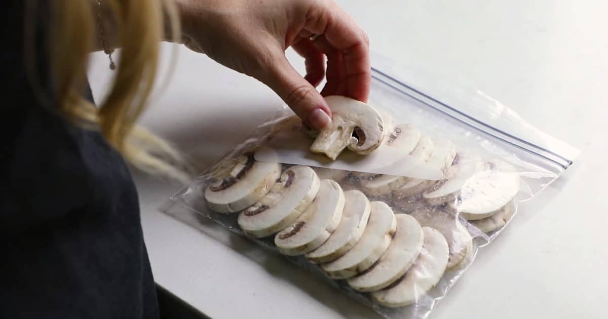 main de femme disposant des champignons de paris en tranches dans un sac de congelation transparent