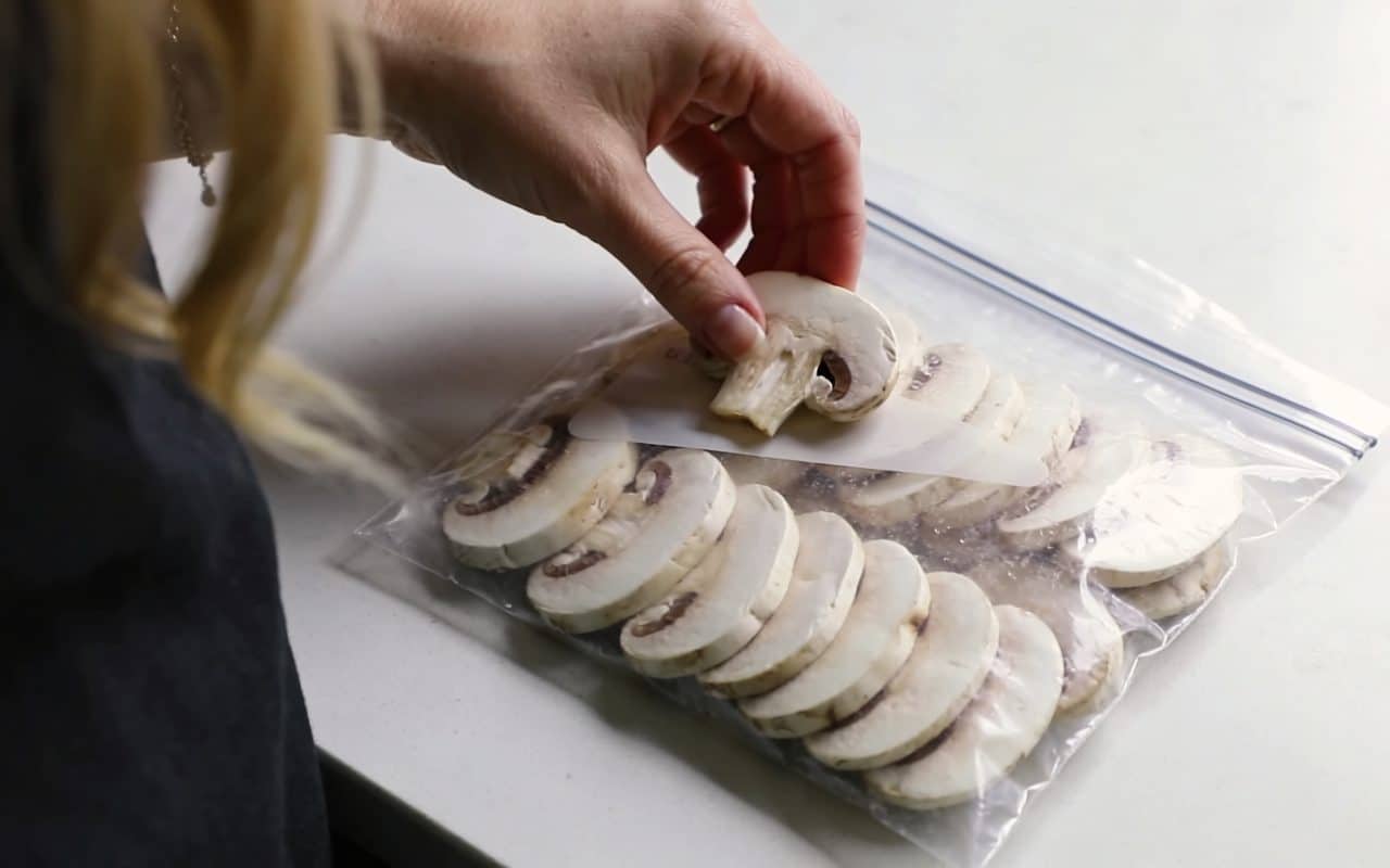 main de femme disposant des champignons de paris en tranches dans un sac de congelation transparent