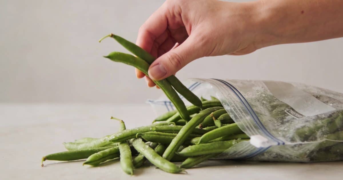Main de femme plaçant haricots verts crus dans sac congelation