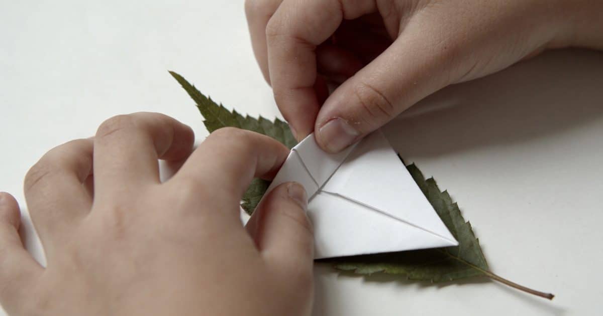 Mains denfant pliant une feuille blanche en origami