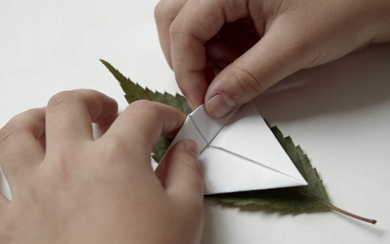 Mains denfant pliant une feuille blanche en origami