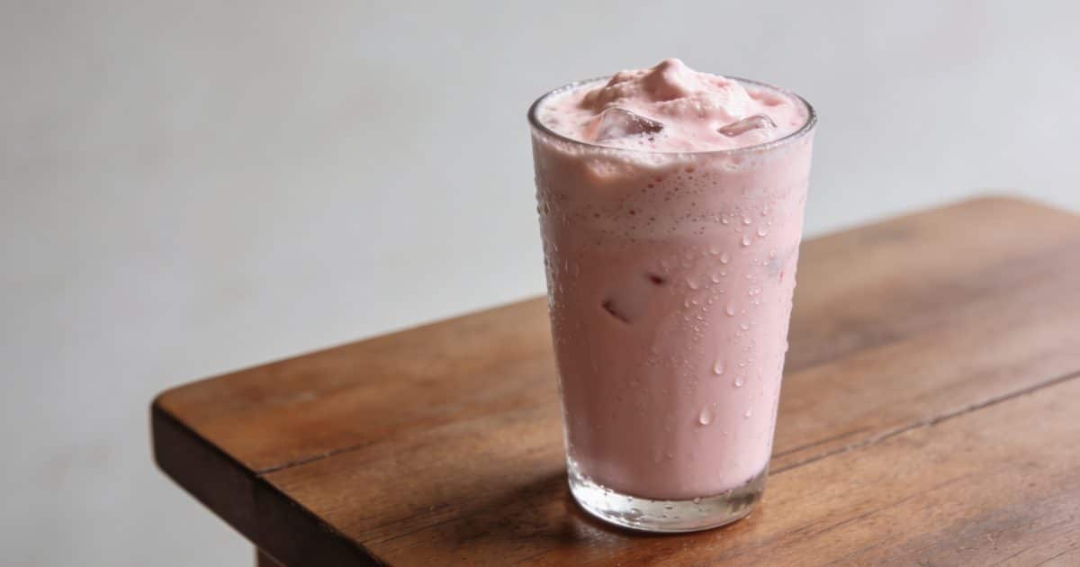 Verre de boisson rose frappee sur table en bois