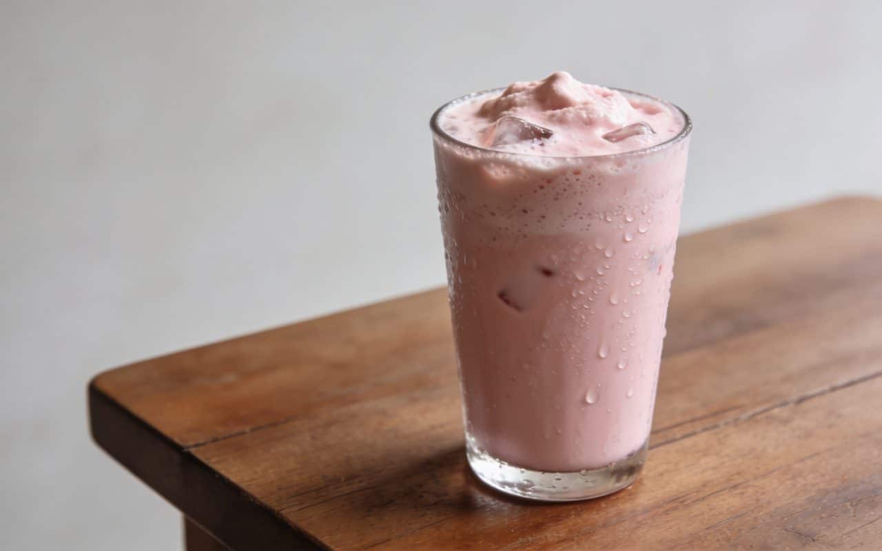 Verre de boisson rose frappee sur table en bois