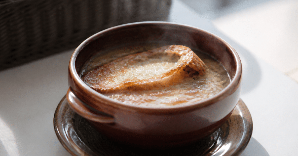 Bol de soupe à l'oignon fumante posé sur table blanche